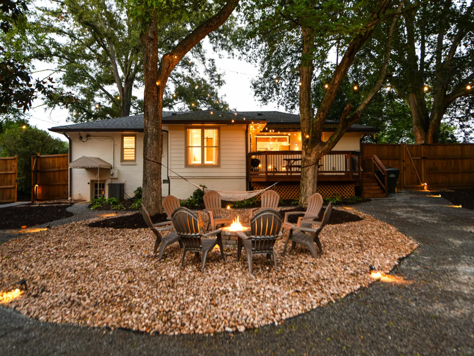 Shared fire pit circle with the back of the Crossing House and its deck lit up behind it at dusk