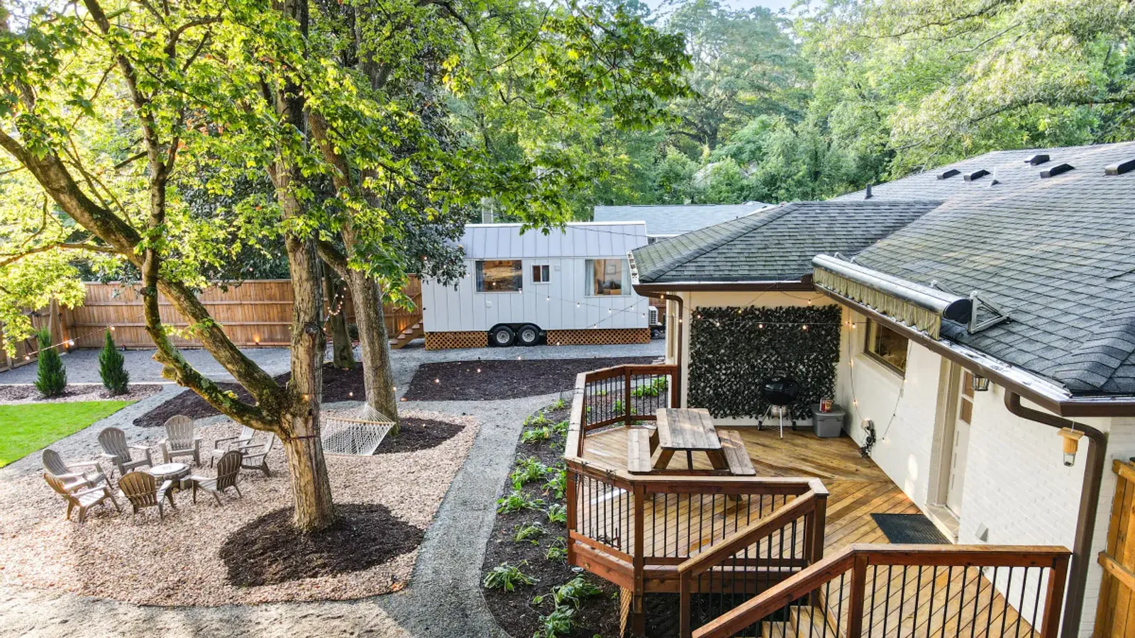 Aerial view of the shared yard: the Crossing House deck and picnic table on the right, the Magnolia Mini behind the trees and the fire-pit circle and hammock on the left