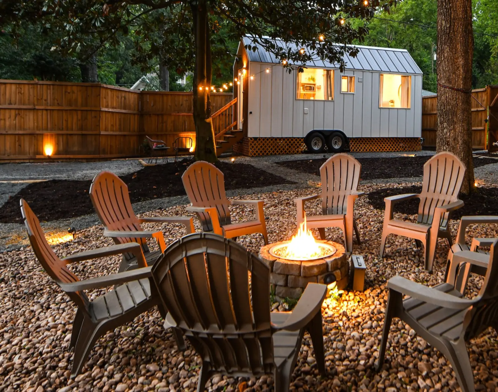 The Magnolia Mini tiny home glowing behind the fire pit at dusk