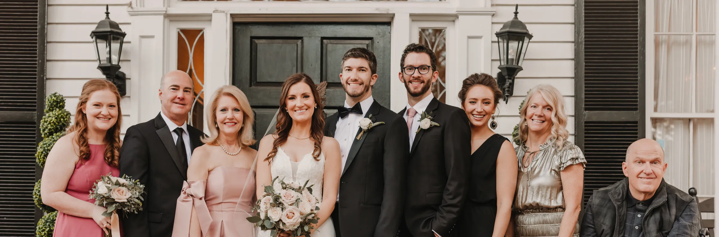 The bride and groom with family on the wedding day, in front of a house with lanterns by the door